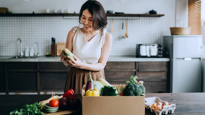 Smiling woman in the kitchen unpacking a box of fresh produce