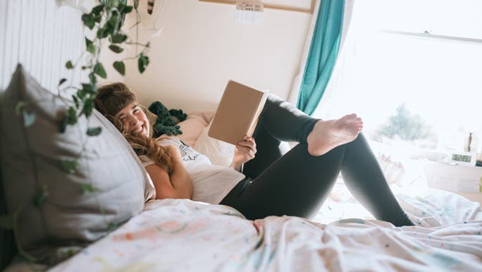 Smiling young woman lying on her bed with a book
