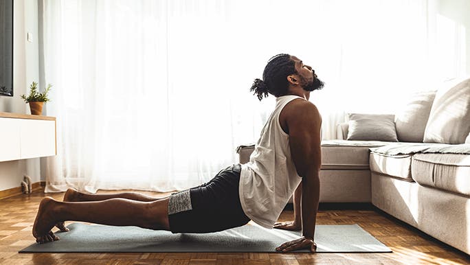 A man practices yoga in his home. He is in cobra pose.