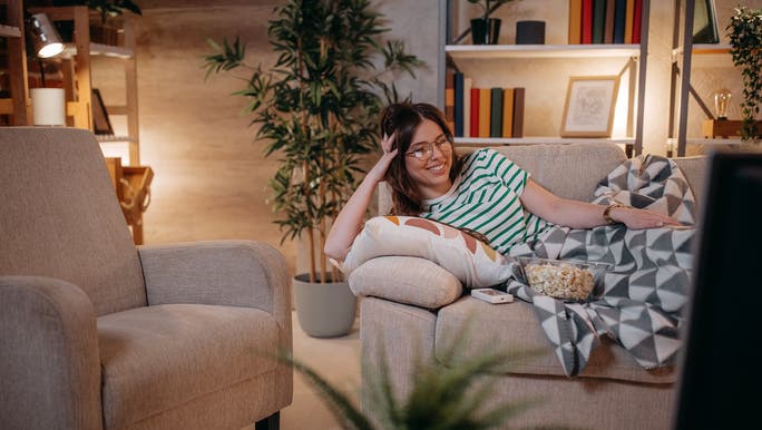 A woman is smiling as she relaxes on a sofa in a cosy home