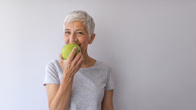 A lady is enjoying an apple, she is choosing healthy food over a fad diet. 