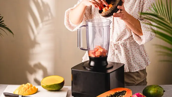 Woman adding summer fruits to a blender