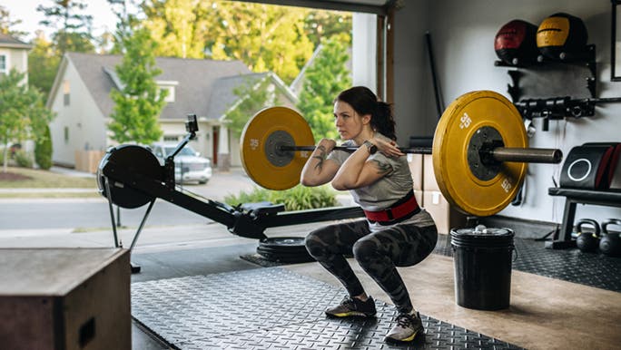 A woman is about to lift a barbell in front of the best home gym equipment she owns in Australia.