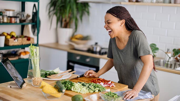 Happy woman in the kitchen laughing and chopping vegetables