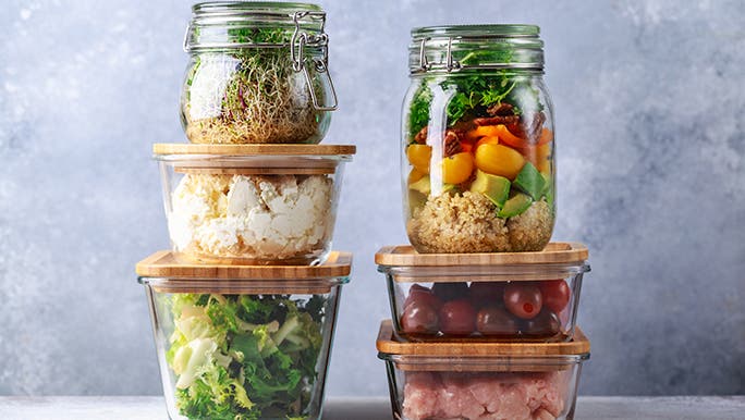 Glass containers of all different kinds are stacked on top of each other. They all have cooked veggies in them. 