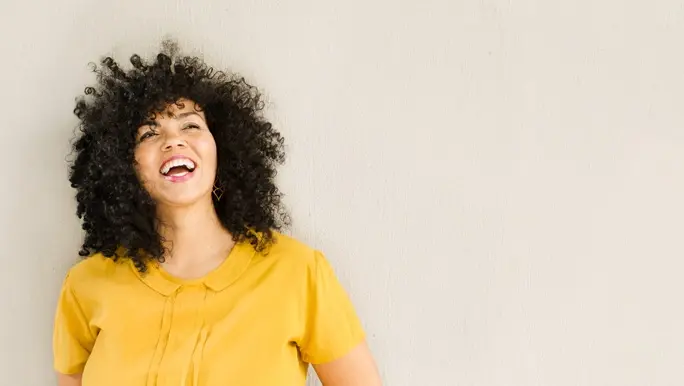 Happy, laughing woman in a yellow shirt with thick curly dark brown hair