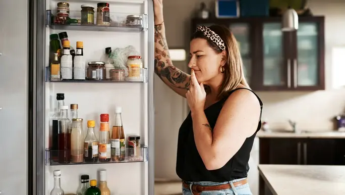 Woman in jeans and a black tank top looking in the fridge for something to eat