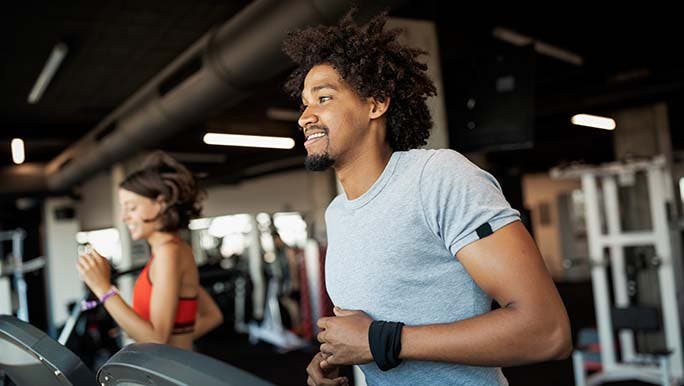 Man smiles while running on a treadmill thinking about how often you should go to the gym.