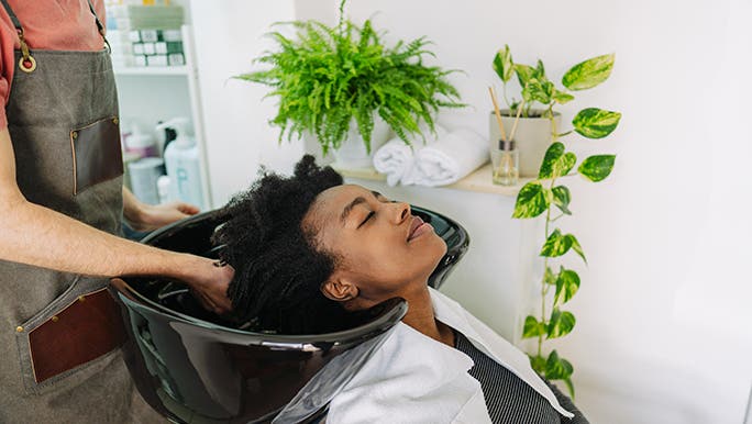 A lady leans back and enjoys having her curly hair shampooed in a salon sink. 