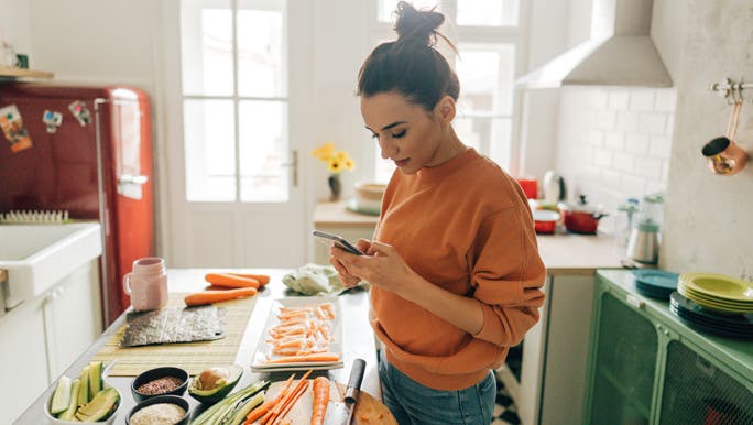 Woman looking at her phone in the kitchen preparing sushi