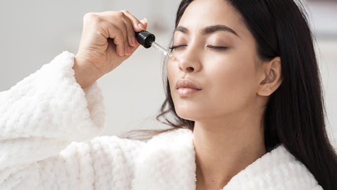 With her eyes closed, a woman is applying a face serum to enjoy the benefits