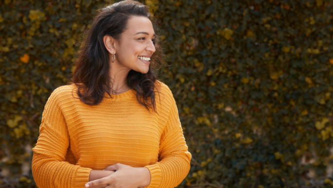 A woman is smiling and has her hands placed over her stomach, indicating she has a happy gut.