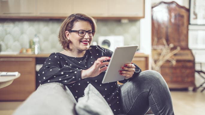 A life coach sits on a lounge with an iPad in her hand. She is explaining to her client what a life coach does. 
