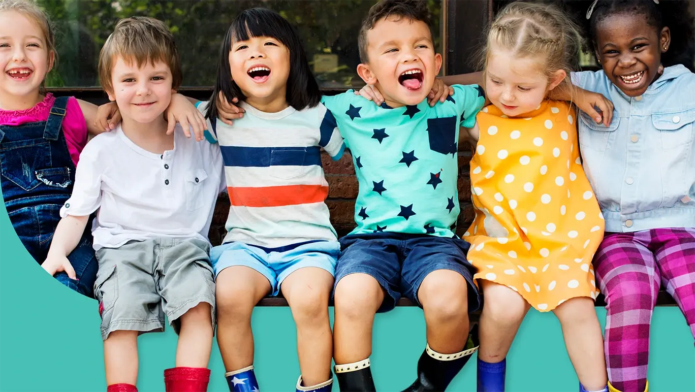 Happy kindergarten age boys and girls sitting together on a bench with their arms around each other
