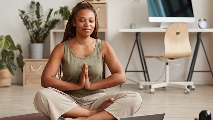 A woman sits in her office doing a ten minute morning yoga practice. 