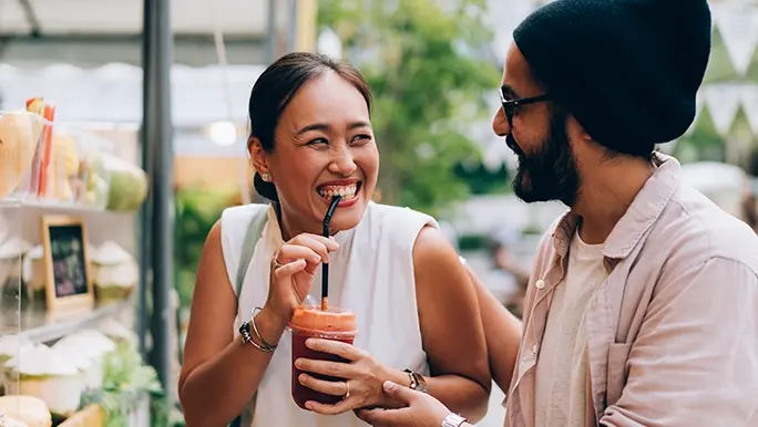 Woman sips on a fresh juice while at the farmer's markets with her male companion.