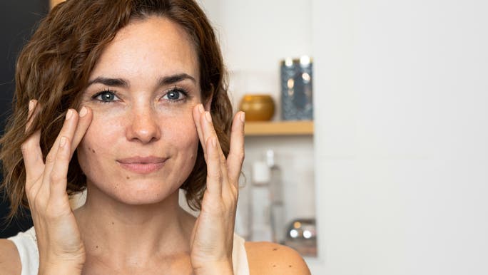 Young woman with wavy brown hair examining her skin in the mirror