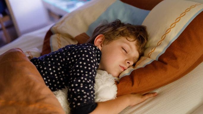 A young boy is sleeping in a cosy bed and hugging a white fluffy toy