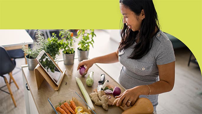 Woman chopping vegetables and following a recipe on her ipad in the kitchen
