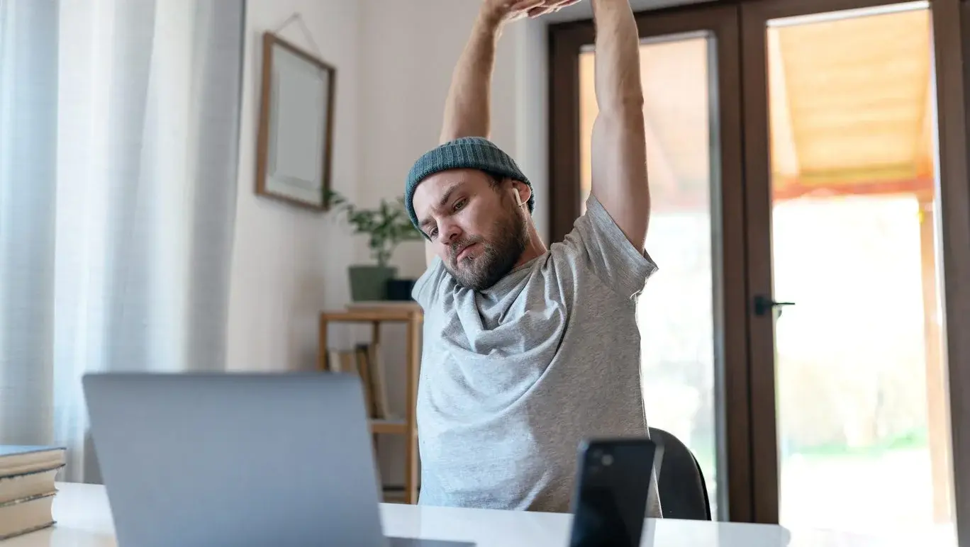 Man stretching at his desk whilst working from home