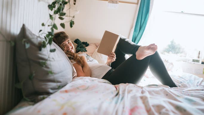 Happy young woman relaxing on her bed reading a book