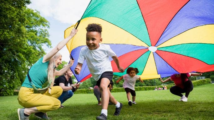 Young children are running underneath a colourful cloth