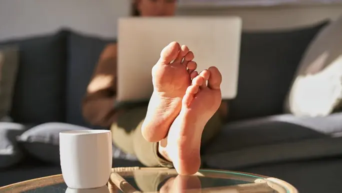 Woman working on her laptop on the couch with her feet up on the coffee table