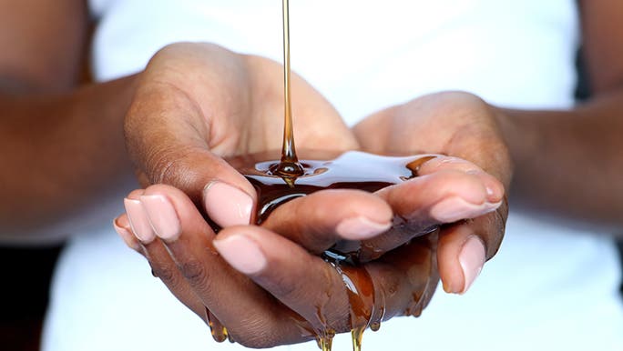 Two hands cradle honey dripping from above as manuka honey is good for skin care.