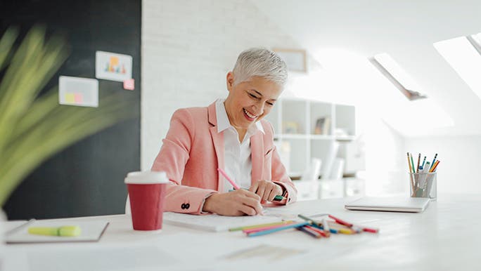 A woman in a bright office smiles as she does her work with colourful markers. 