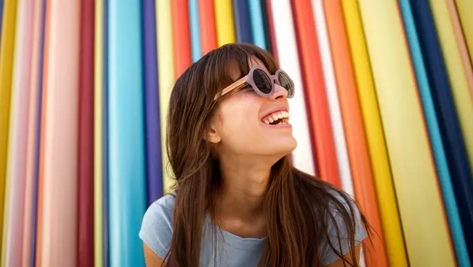 Cheerful young woman laughing with sunglasses against colourful background 