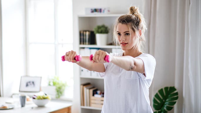 A woman works out in her home with small, pink weights. She is wondering how much exercise she should do per week.