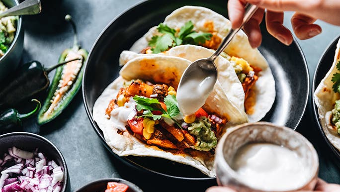 From above, someone is drizzling white sauce on some plant based or vegan nachos. 