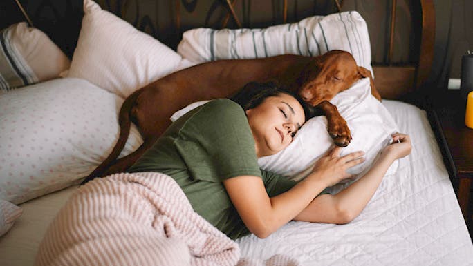 A young woman wearing a green T-shirt is seeping with her dog