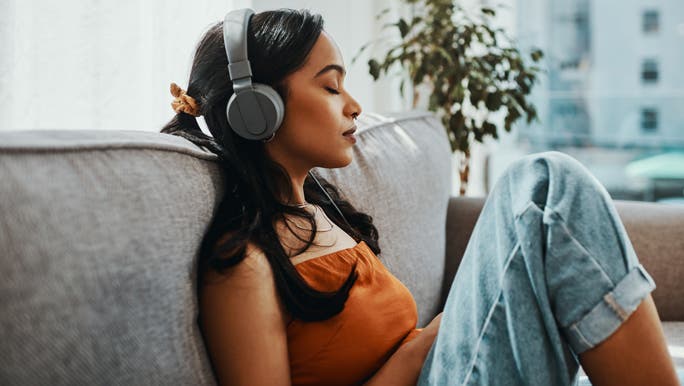 Young woman using headphones while relaxing on the lounge at home