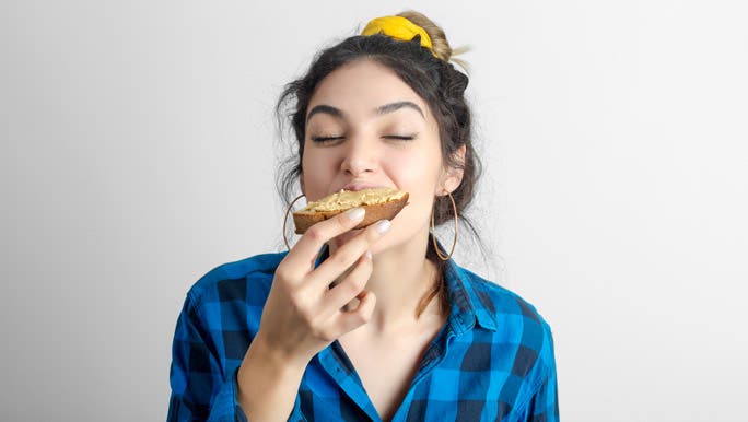 Young woman in a blue check shirt enjoying peanut butter on toast