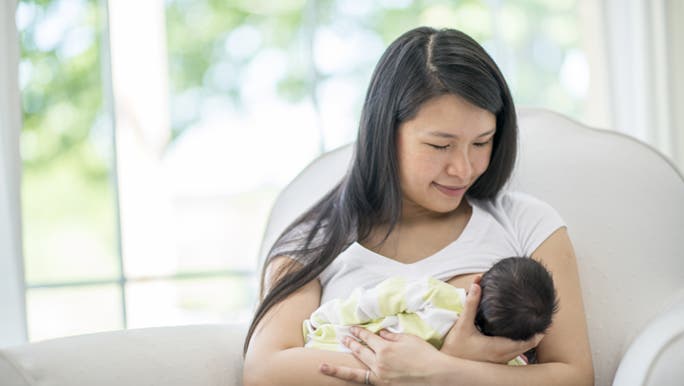 A woman smiles while breastfeeding her child as she just learned some breastfeeding tips.  