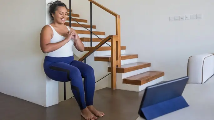 Woman working out at home, doing a wall sit