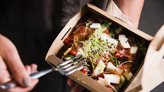 A fork is digging into a healthy takeaway salad full of sprouts, feta and tomatoes. 
