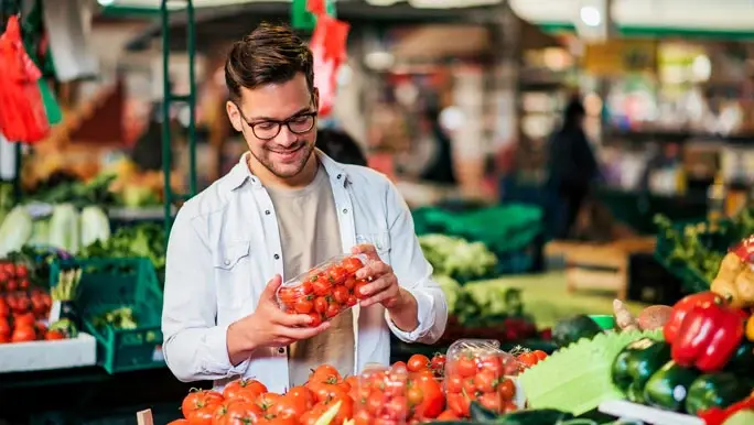 Man at the farmers market looking at a punnet of cherry tomatoes