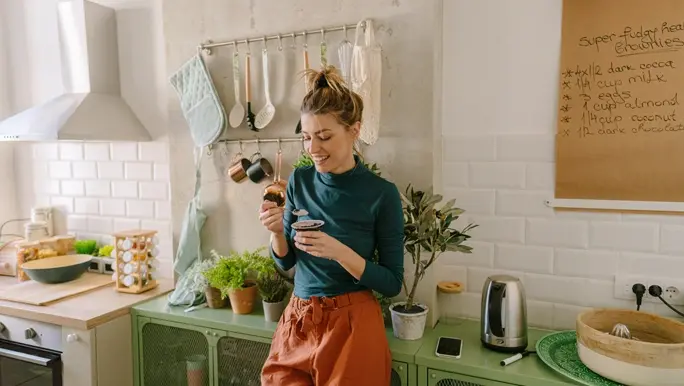 Young smiling blonde woman having healthy snack in her kitchen