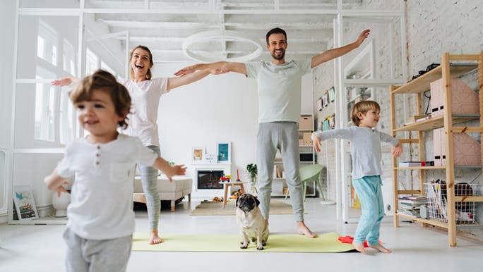 A family is taking part in a fitness challenge - the parents are doing stretches while the kids run around them. 