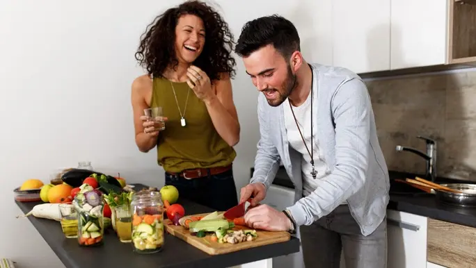 Young couple in kitchen preparing a meal with a variety of vegetarian ingredients.