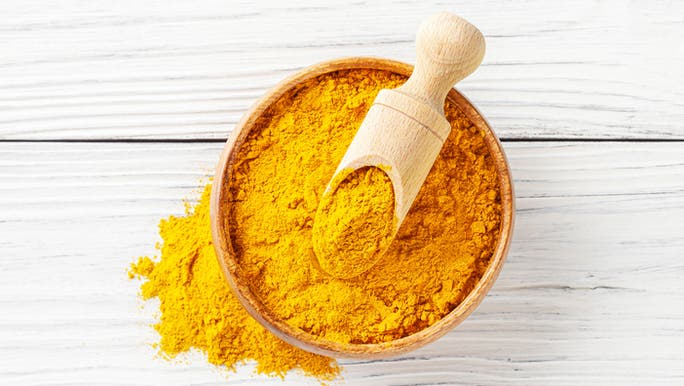 A bowl of turmeric powder containing a wooden scoop