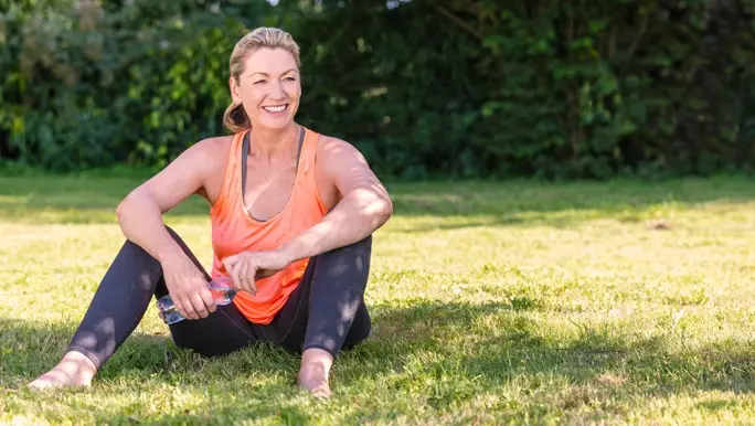 Blonde woman in activewear smiling and sitting in the shade in the park