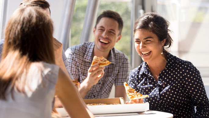 A group of office workers sharing a pizza at a table and laughing 