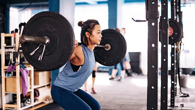 A woman holds a weighted barbell above her head in the gym while doing weight training.