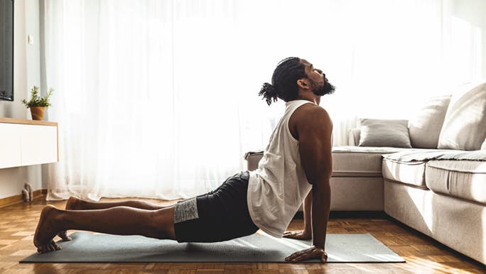 A man is doing yoga at home on a mat and wonders if there are some good free yoga classes online. 