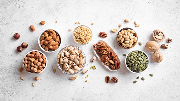 Various nuts are in bowls laid out on a white background. 