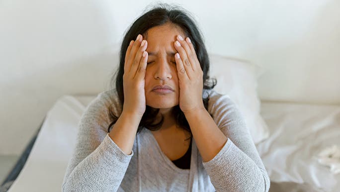 Woman sitting on a bed holds her face in her hands, she is experiencing menopause and sleep issues. 