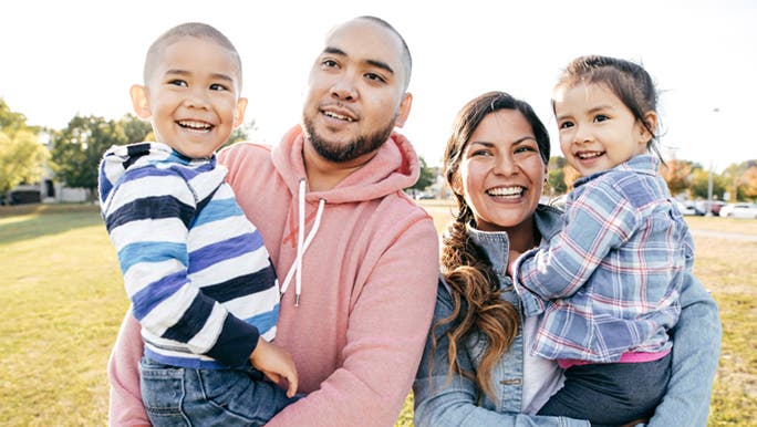 A family with two young children are enjoying the park. It's a sunny but cold day. 